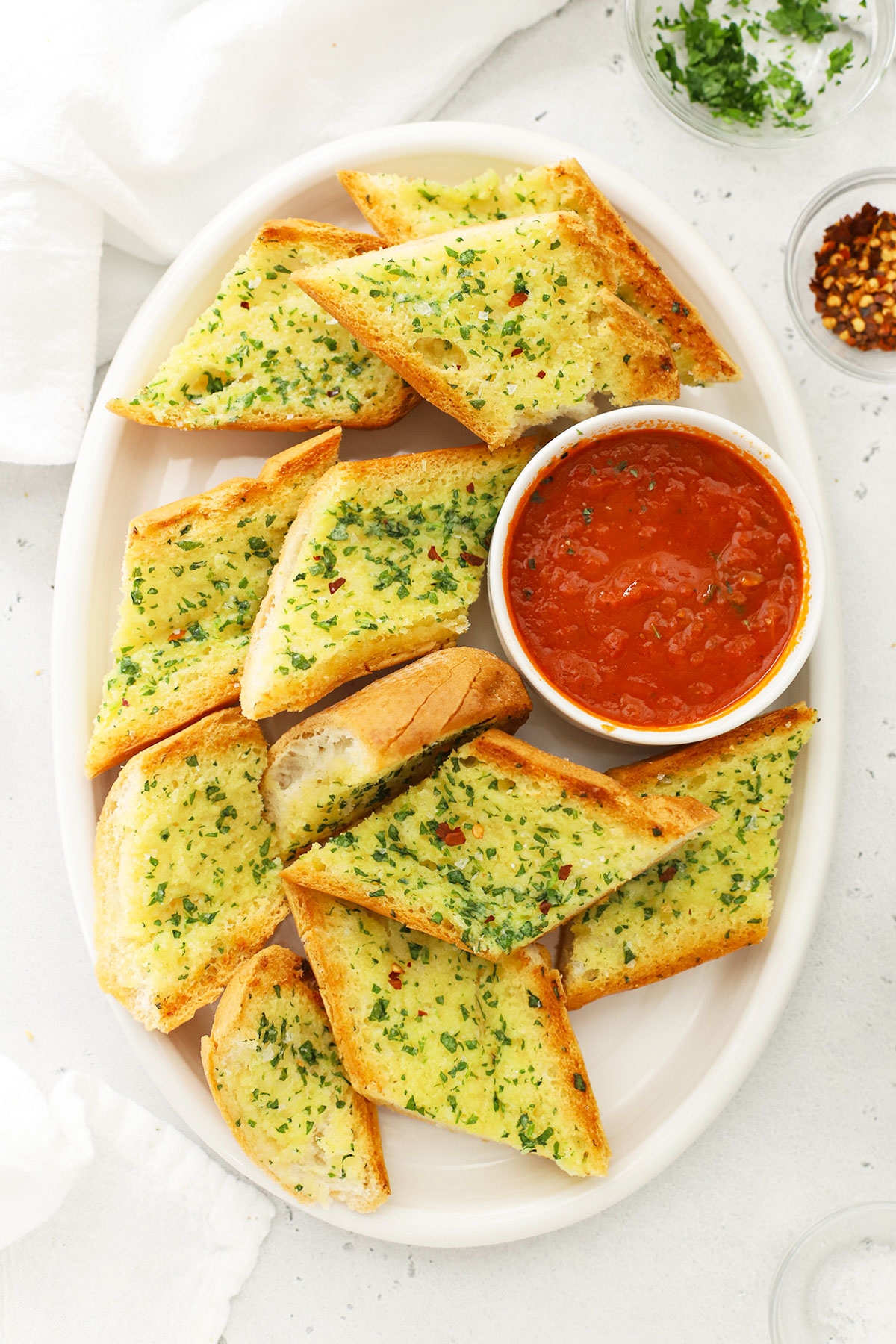 Overhead view of slices of garlic bread on a white platter with a bowl of marinara sauce