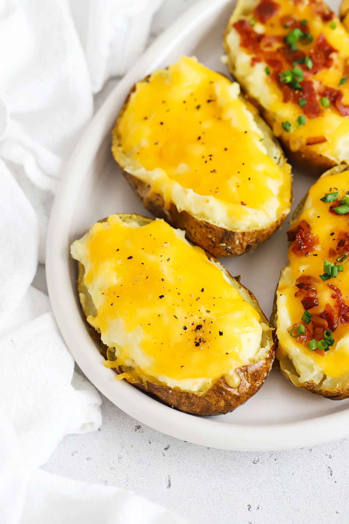 Stuffed twice baked potatoes with cheese, bacon, and chives on a white plate