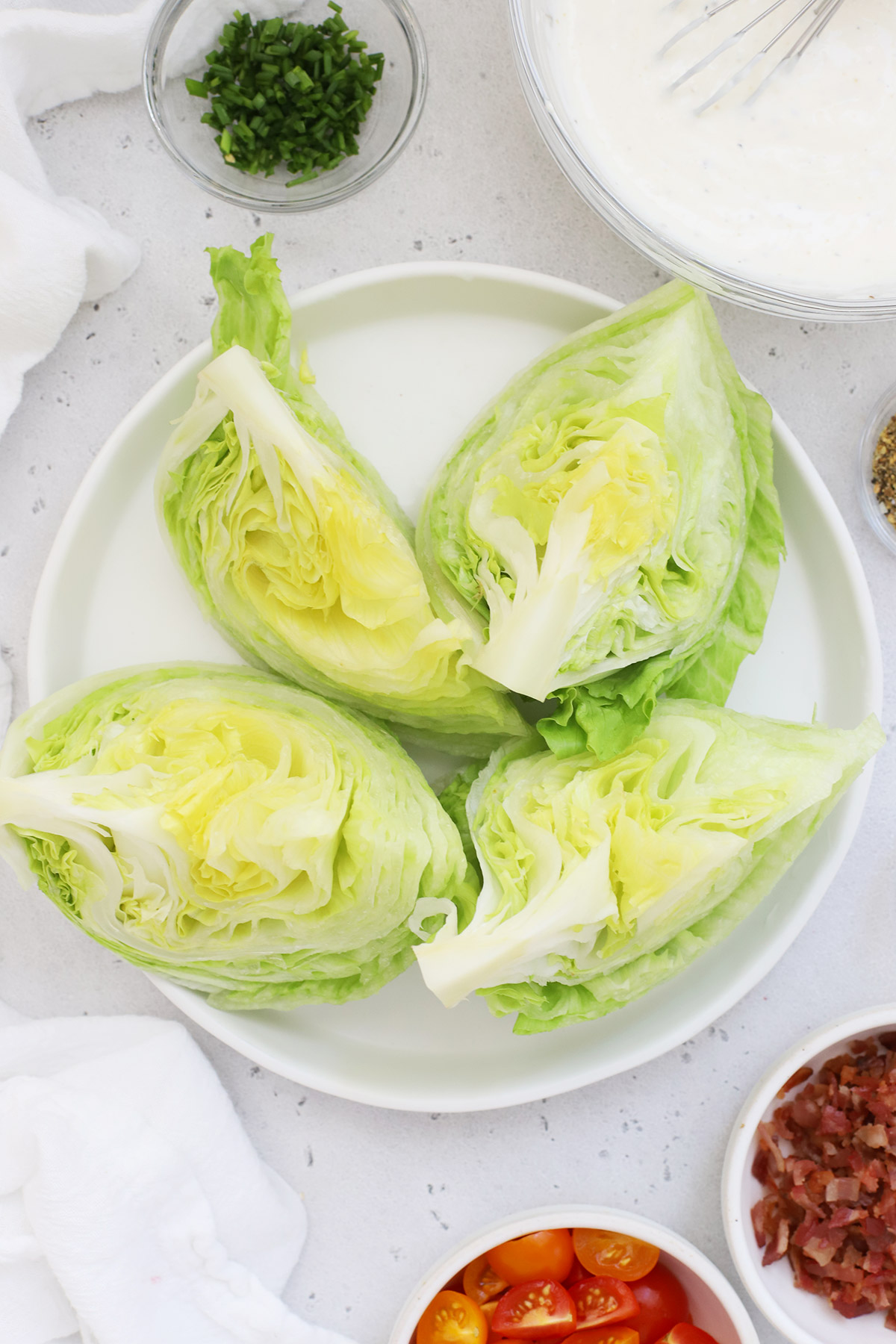 lettuce wedges on a white plate surrounded by wedge salad toppings