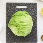 a whole head of iceberg lettuce on a black cutting board