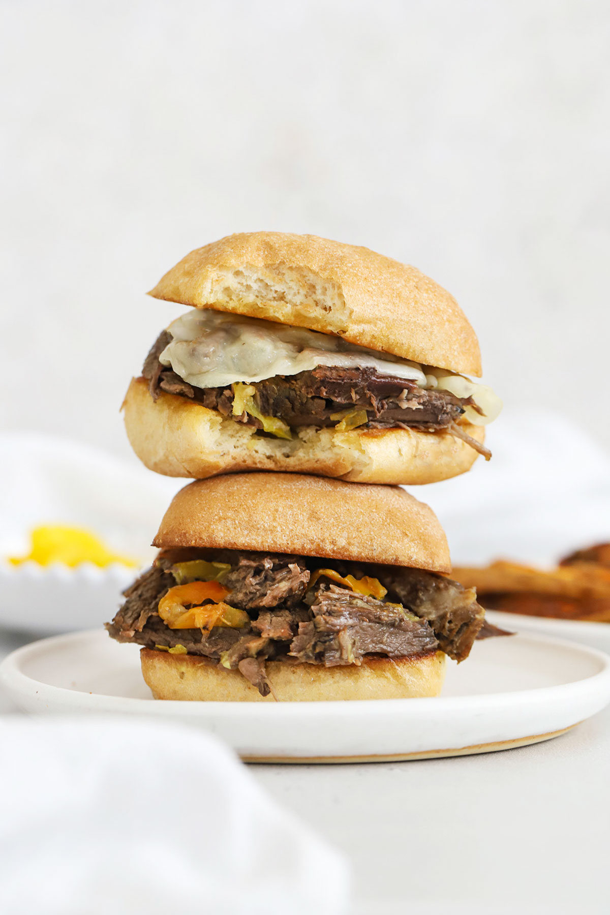 Slow cooker Italian beef sandwiches with peperoncini stacked on a white plate