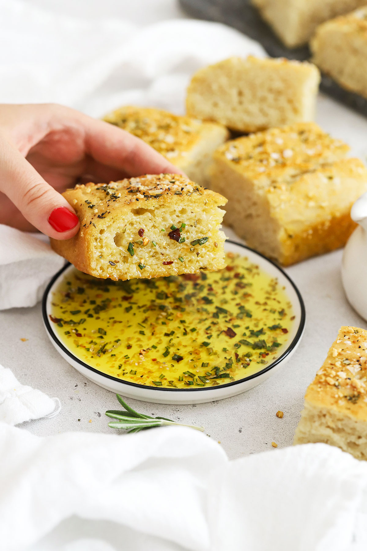 Gluten-free focaccia bread being dipped into herbed olive oil