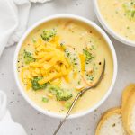 overhead view of a bowl of creamy gluten-free broccoli cheddar soup on a white background