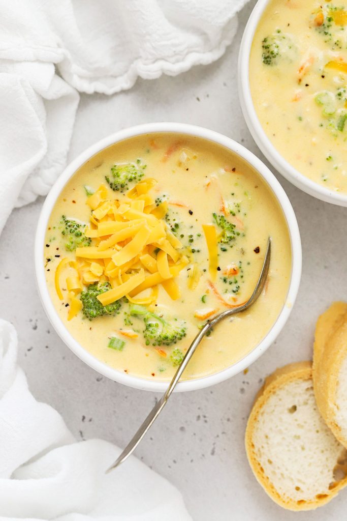 overhead view of a bowl of creamy gluten-free broccoli cheddar soup on a white background