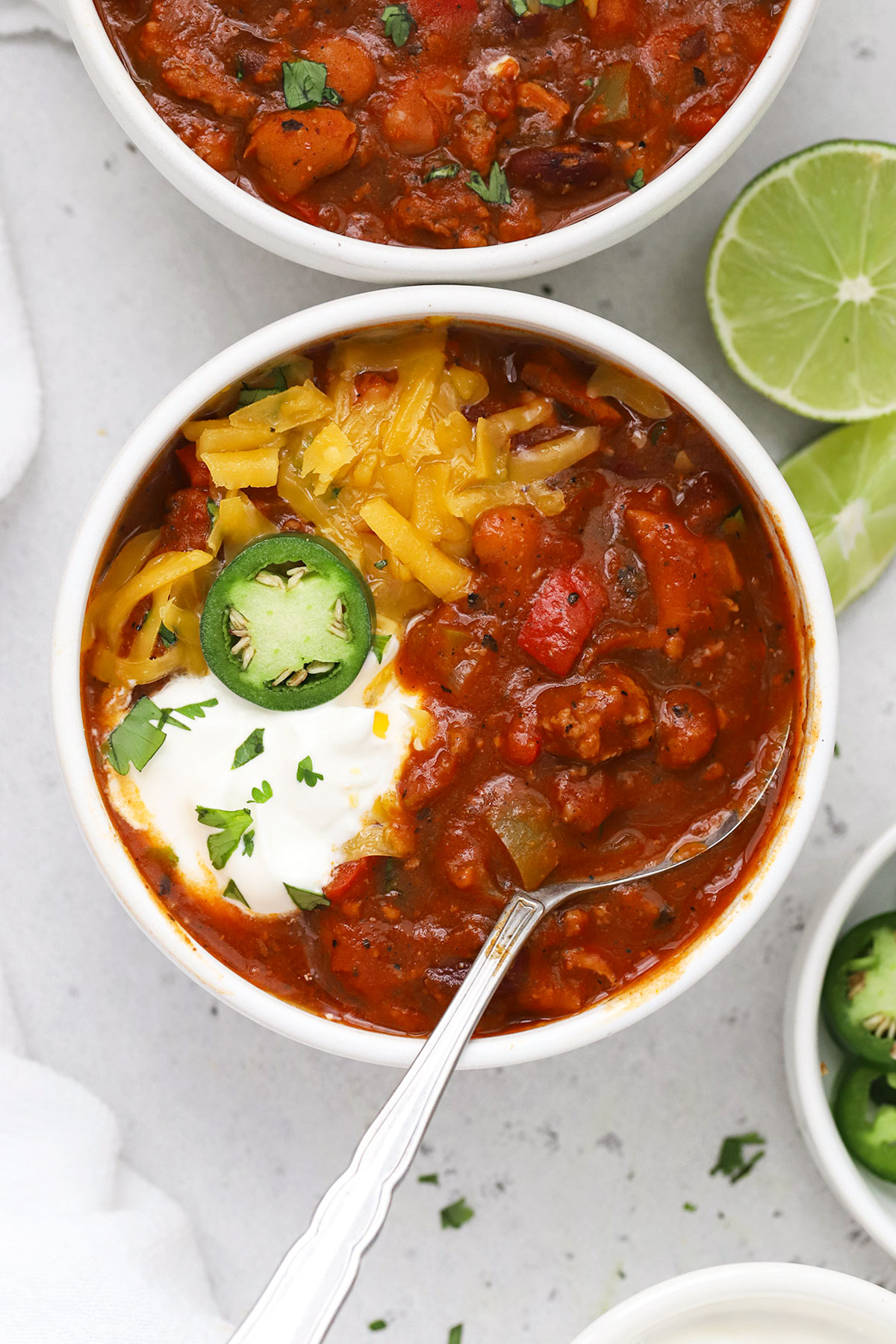 a bowl of gluten-free chili topped with sour cream, cheddar cheese, and jalapeño