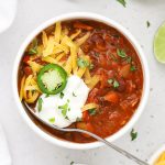 a bowl of gluten-free chili topped with sour cream, cheddar cheese, and jalapeño