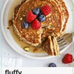 gluten-free oatmeal pancakes stacked on a white plate, topped with fresh berries and maple syrup