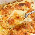 scooping gluten-free scalloped potatoes out of a white baking dish