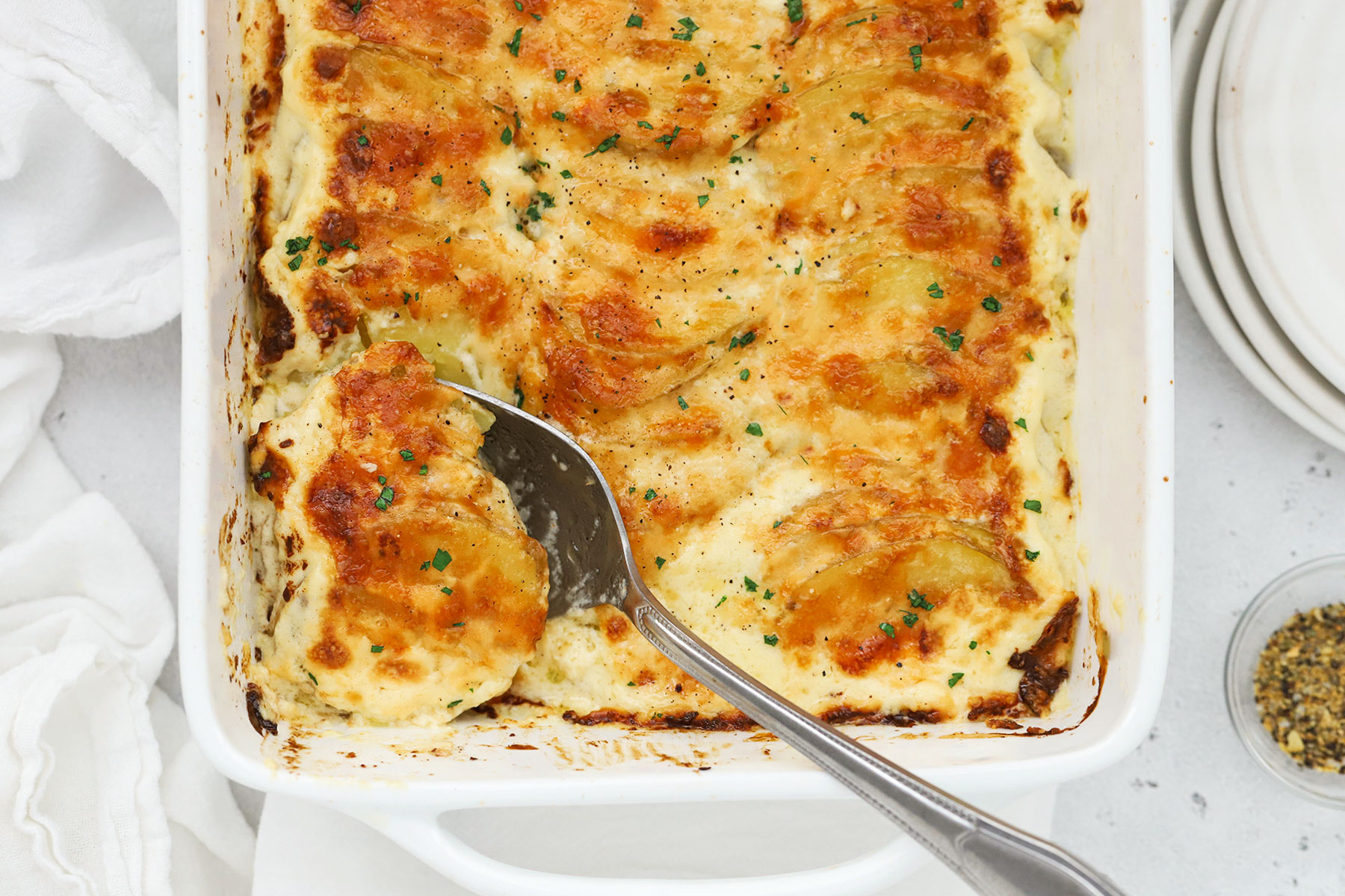 scooping gluten-free scalloped potatoes out of a white baking dish