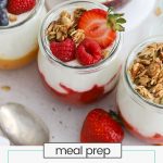 four jars of meal prep fruit on the bottom yogurt topped with granola and berries