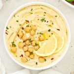homemade lemon hummus in a white bowl topped with fresh herbs and chickpeas