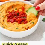 dipping a cucumber into roasted red pepper hummus