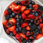 Cherry fruit salad with fresh berries, mint, and honey lime dressing in a white bowl