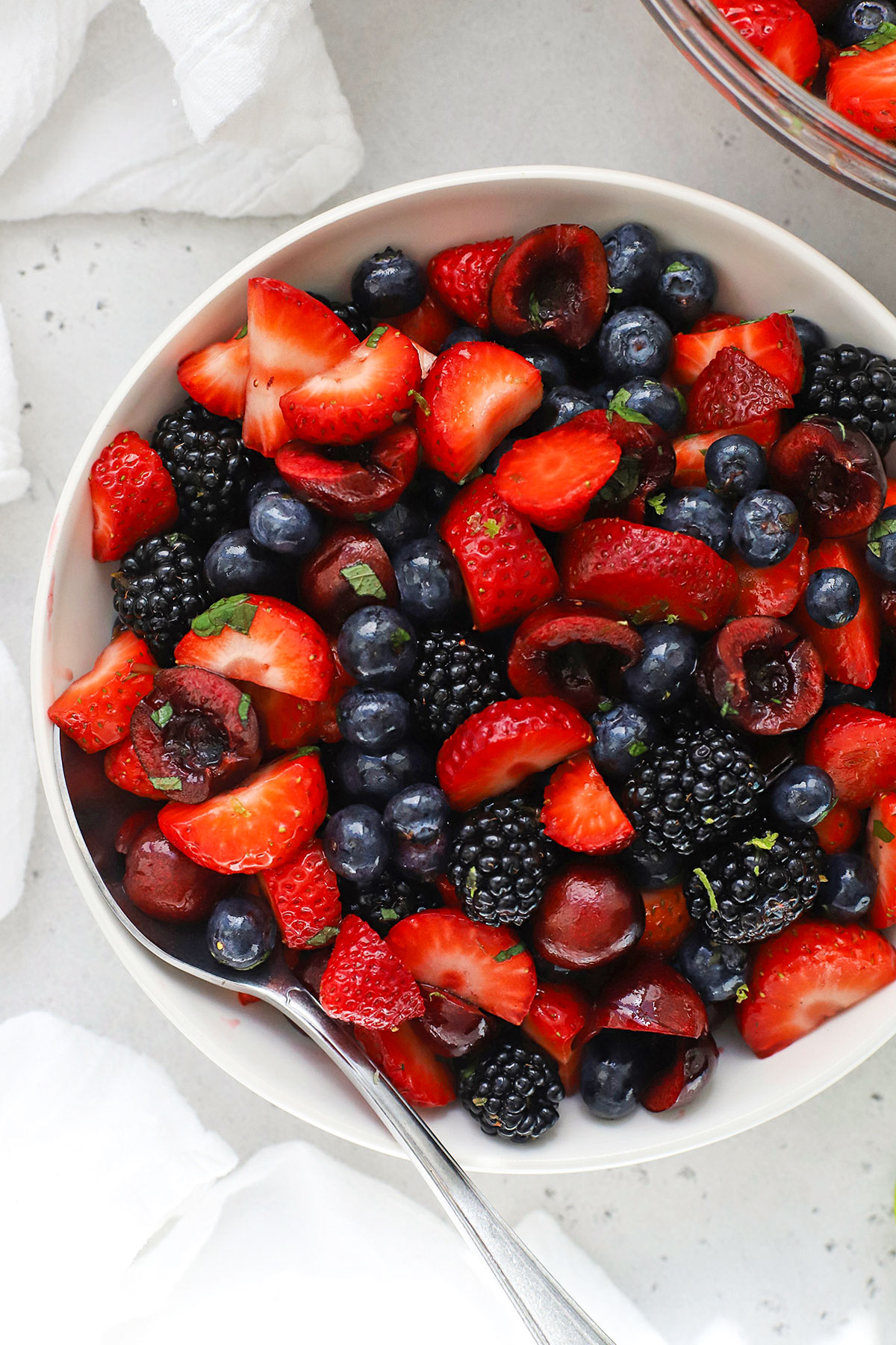 Cherry fruit salad with fresh berries, mint, and honey lime dressing in a white bowl