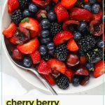 white serving bowl of colorful cherry berry fruit salad with cherries, strawberries, blackberries, and blueberries.