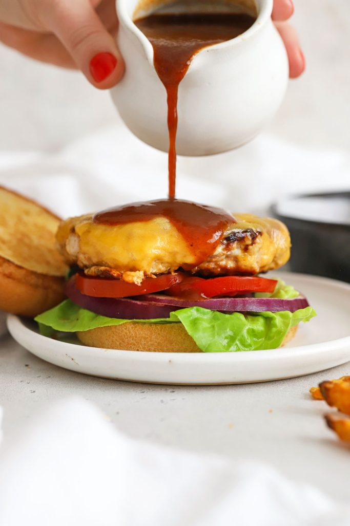 pouring bbq sauce on a healthy chicken cheddar burger