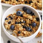 a white bowl of gluten-free blueberry granola with almond milk and fresh blueberries