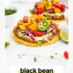 two black bean tostadas topped with guacamole, cilantro lime slaw, fresh mango salsa, and garnishes