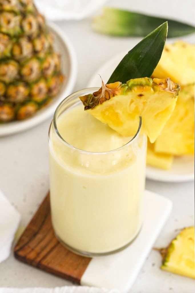 pina colada smoothie in a tall glass with pineapple wedge and pineapple leaf