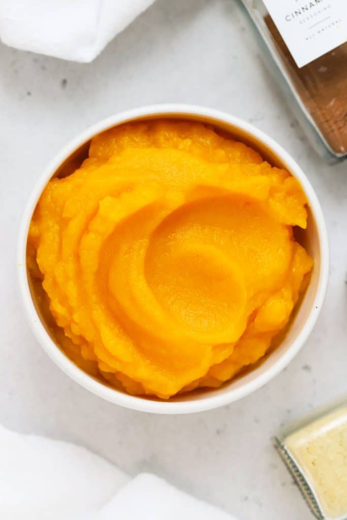 a bowl of homemade pumpkin puree next to jars of spices