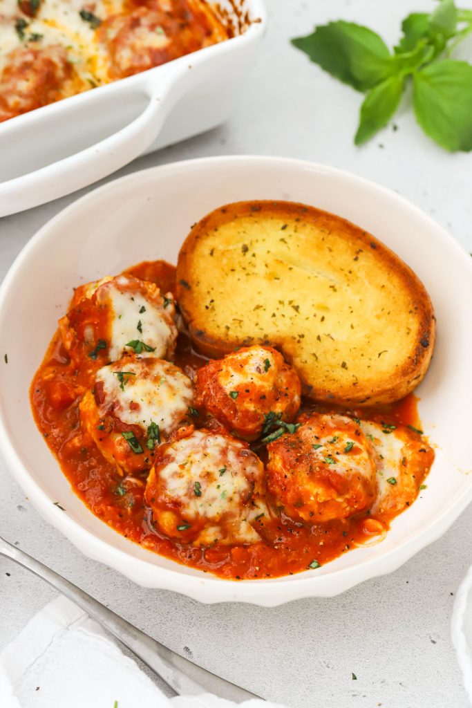 Gluten-free chicken parmesan meatballs in marinara with a slice of gluten-free garlic bread