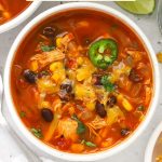 A bowl of cheesy chicken enchilada soup garnished with cilantro and sliced jalapeño