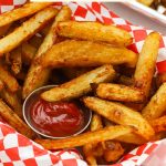 A basked of golden brown seasoned oven fries with a cup of ketchup