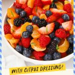 A white serving bowl of orange berry fruit salad