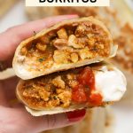 Holding a ground chicken burrito topped with salsa and sour cream