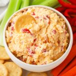 A bowl of homemade pimento cheese dip served with fresh veggies and gluten-free crackers