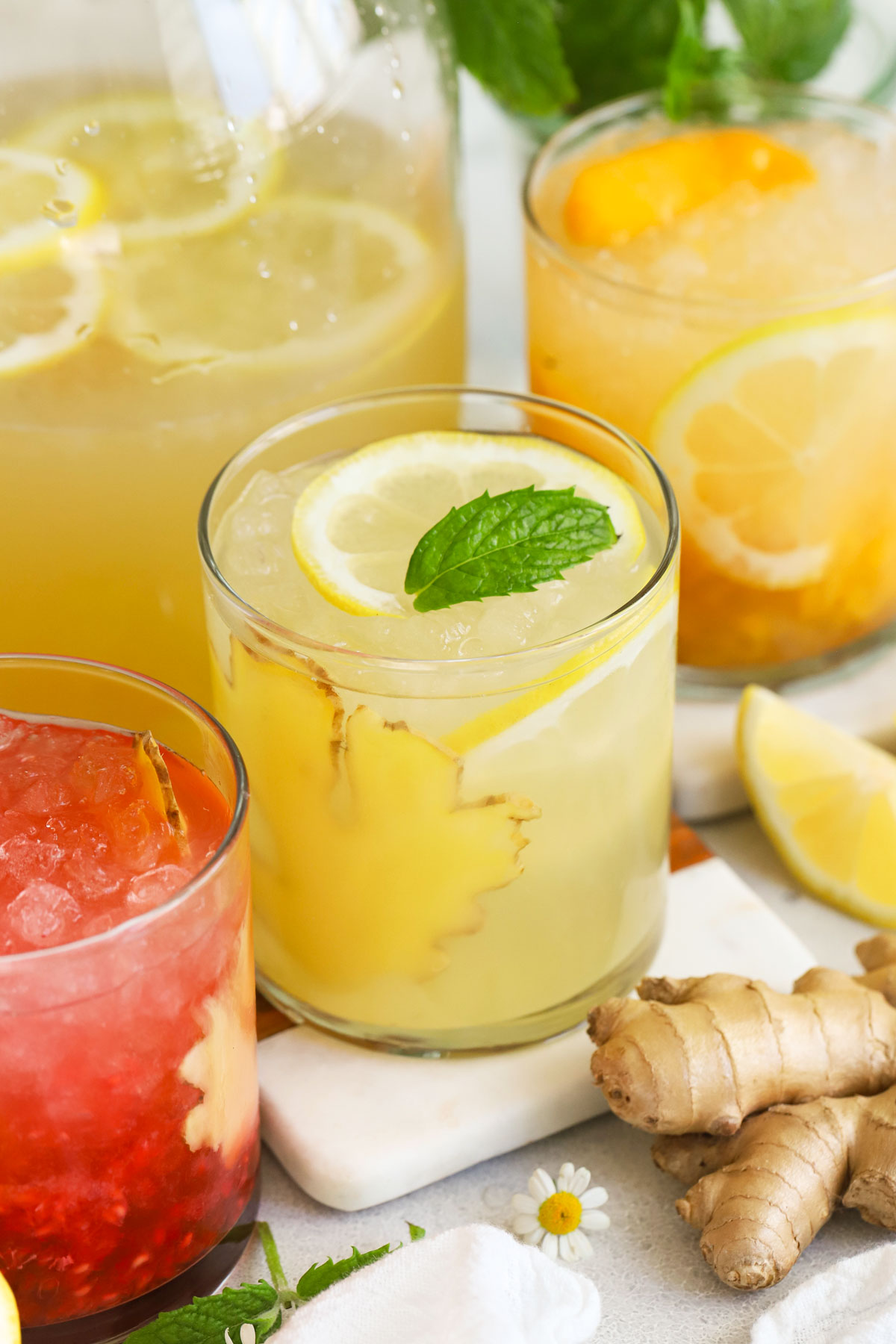 Glasses of honey ginger lemonade garnished with mint, fresh fruit, and slices of ginger