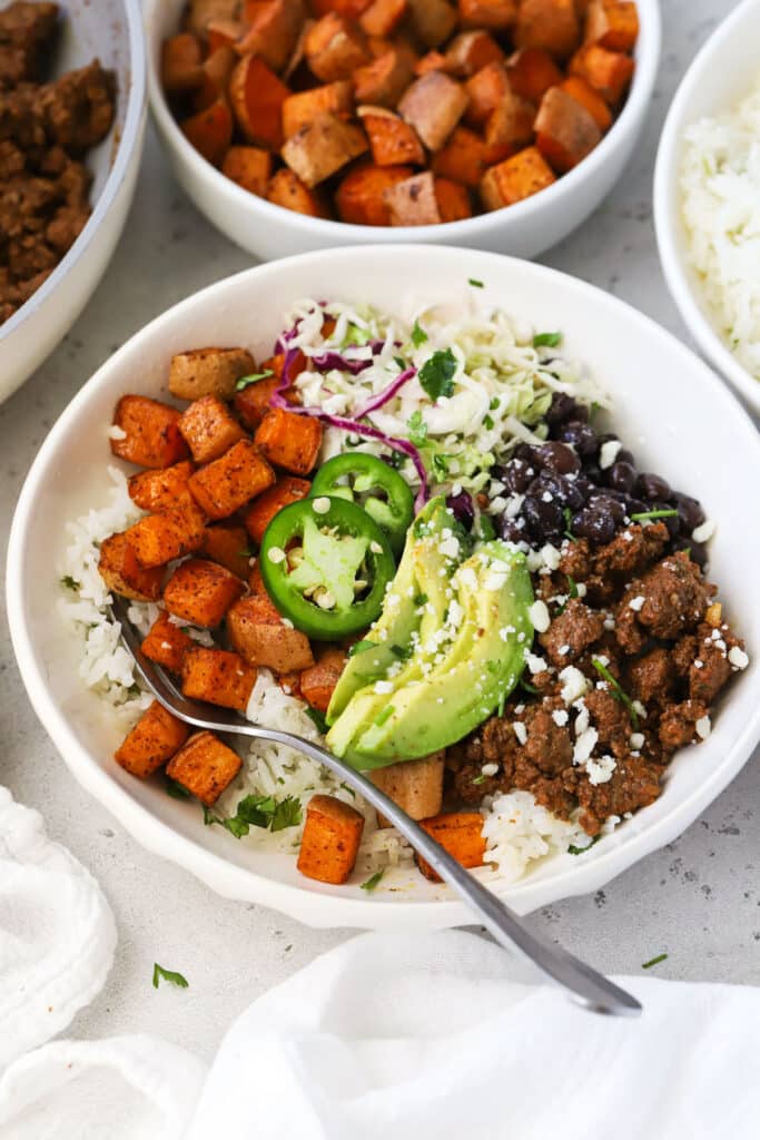 Chipotle beef and sweet potato burrito bowls with avocado slices, black beans, and cilantro lime slaw