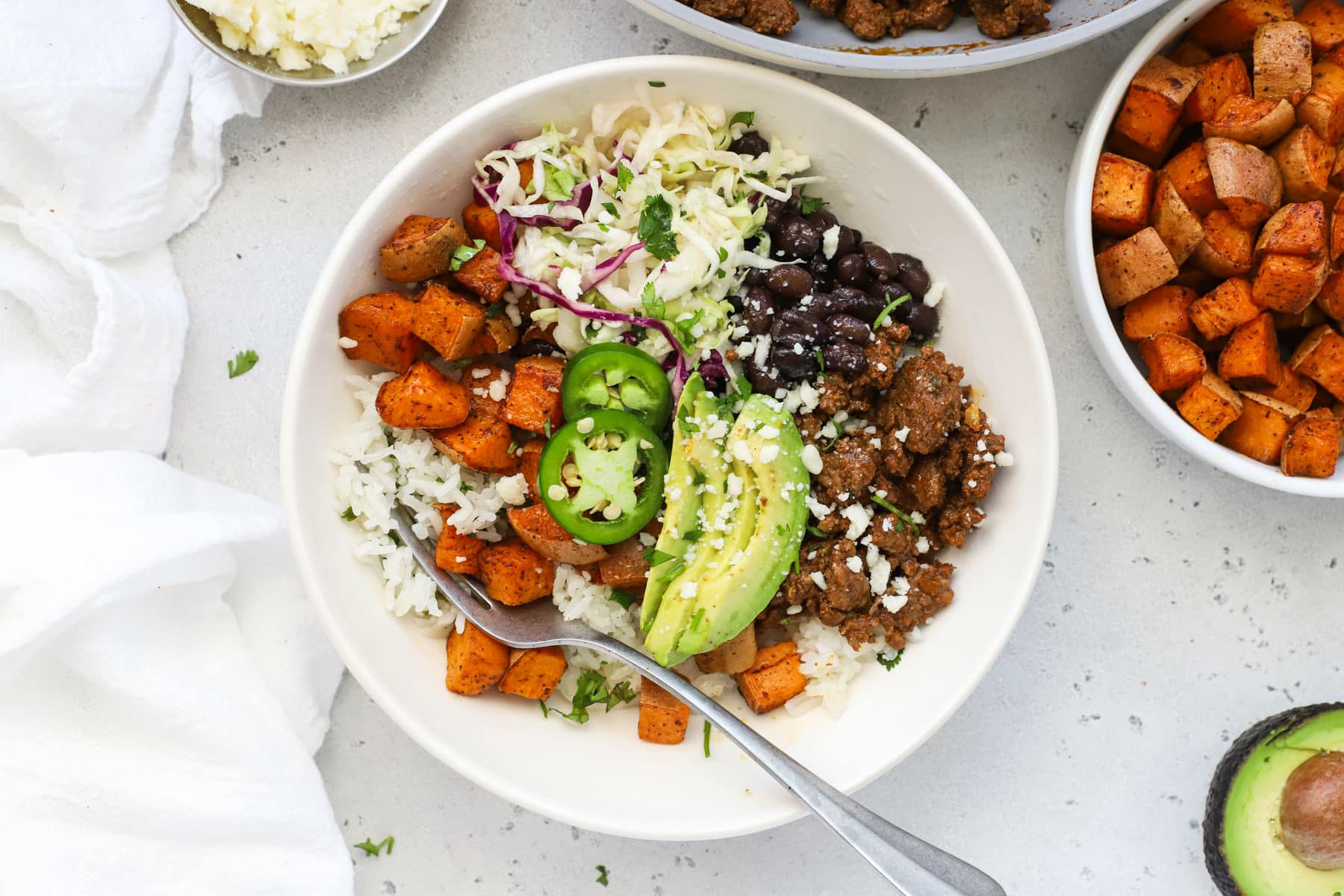Chipotle beef and sweet potato burrito bowls with avocado slices, black beans, and cilantro lime slaw