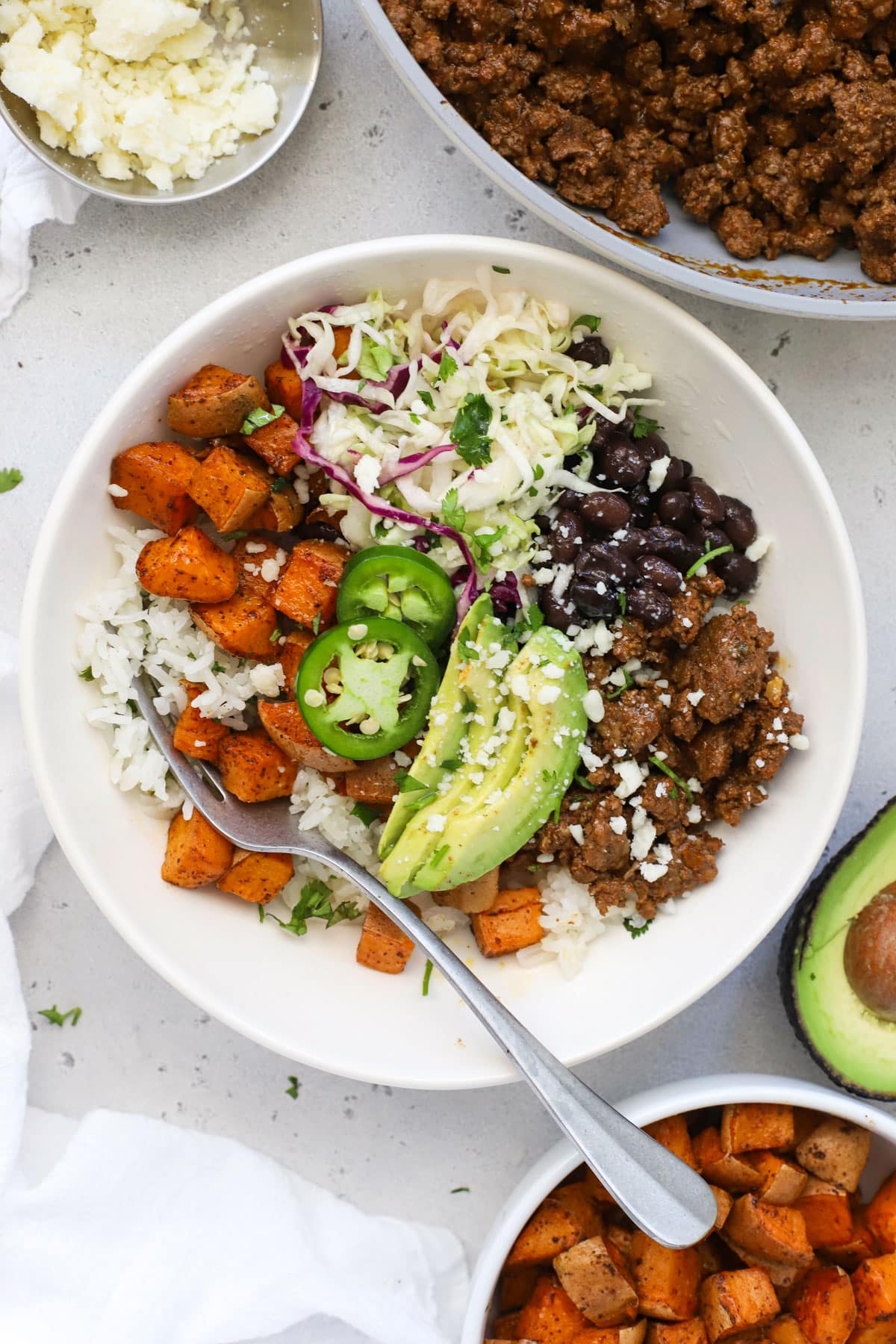 Chipotle beef and sweet potato burrito bowls with avocado slices, black beans, and cilantro lime slaw