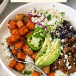 Chipotle beef and sweet potato burrito bowls with avocado slices, black beans, and cilantro lime slaw