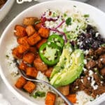 Chipotle beef and sweet potato burrito bowls with avocado slices, black beans, and cilantro lime slaw