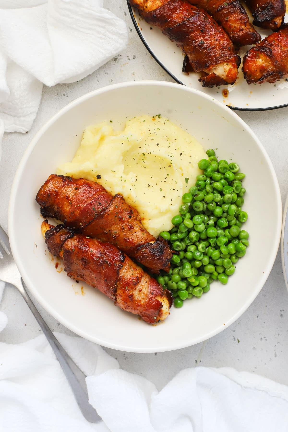 A plate of bacon-wrapped chicken tenders with mashed potatoes and peas