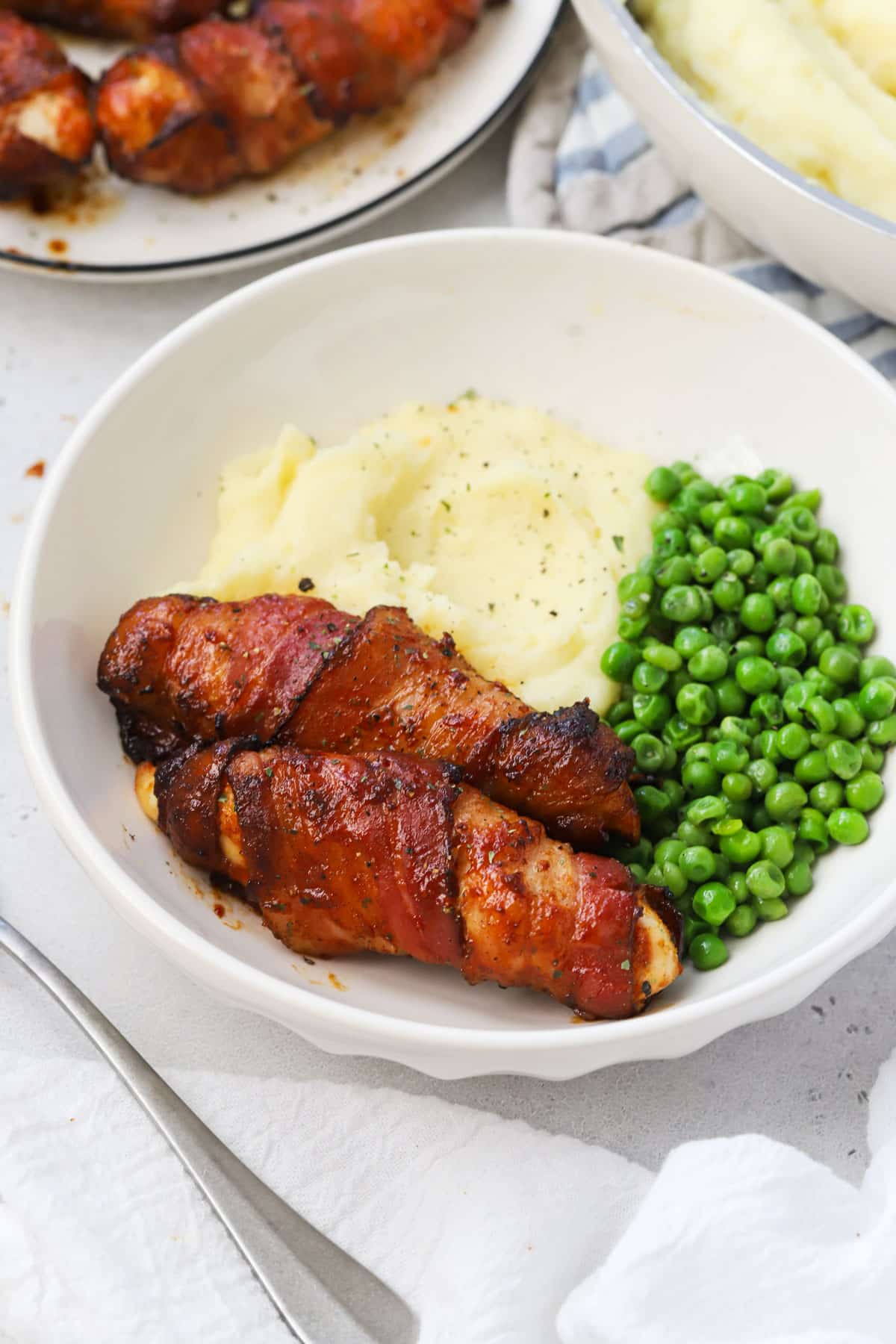 A plate of bacon-wrapped chicken tenders with mashed potatoes and peas