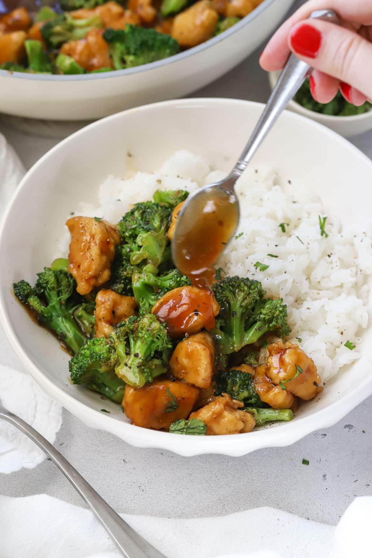 Drizzling sauce over a bowl of chicken & broccoli stir fry