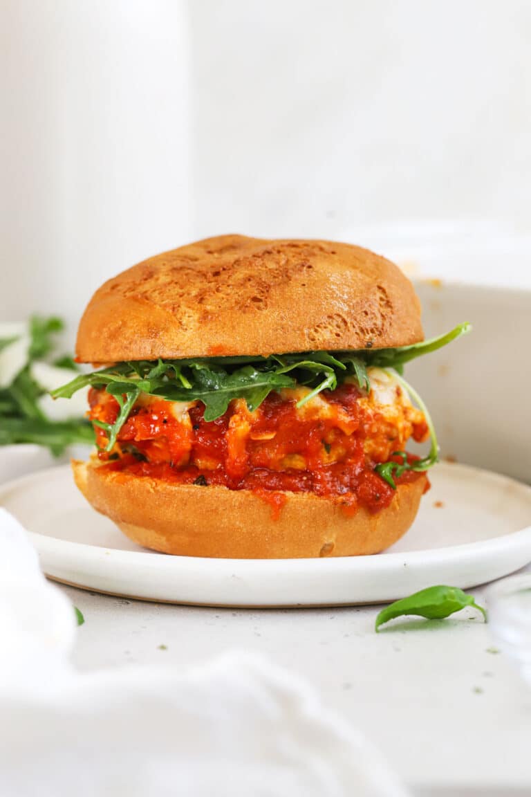 A chicken parmesan burger topped with arugula salad on a white plate
