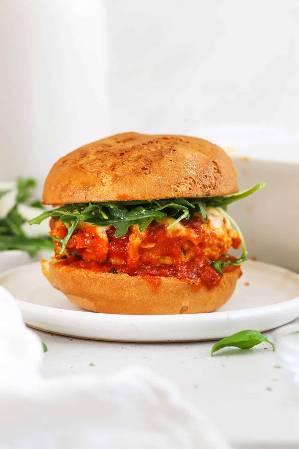 A chicken parmesan burger topped with arugula salad on a white plate