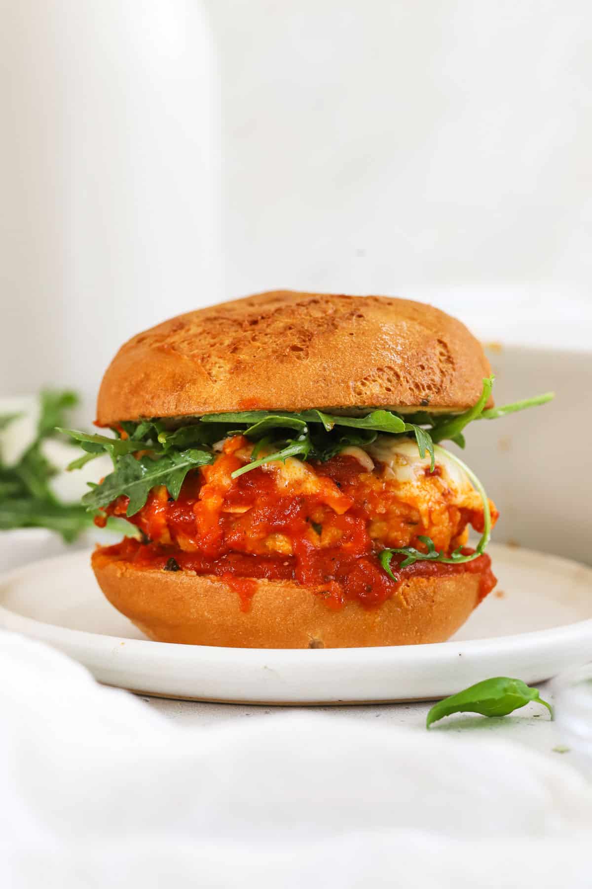 A chicken parmesan burger topped with arugula salad on a white plate