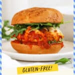 A chicken parmesan burger topped with arugula salad on a white plate